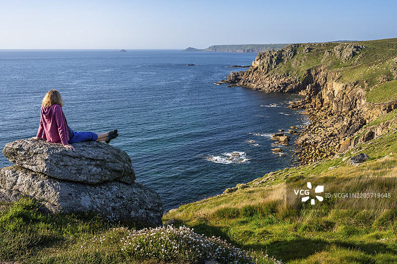 海岸风景在兰兹角。一位徒步旅行者坐在岩石上。兰兹角,彭赞斯,康沃尔,英格兰,英国图片素材