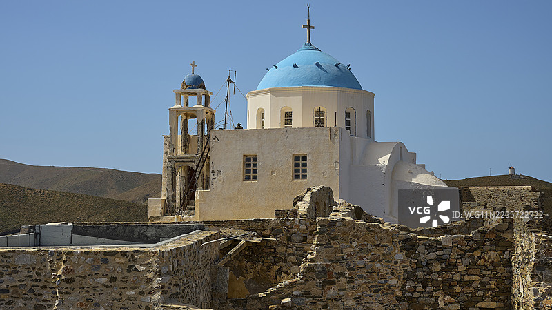 蓝色圆顶教堂与石头遗址相邻，坐落在山脉风景中，蓝天之下，圣母玛利亚福音教堂，霍拉，阿斯提帕利亚，多德卡尼斯群岛，希腊，欧洲图片素材