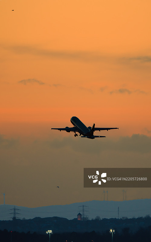 飞机剪影在夕阳下飞过，背景是落日。图片素材