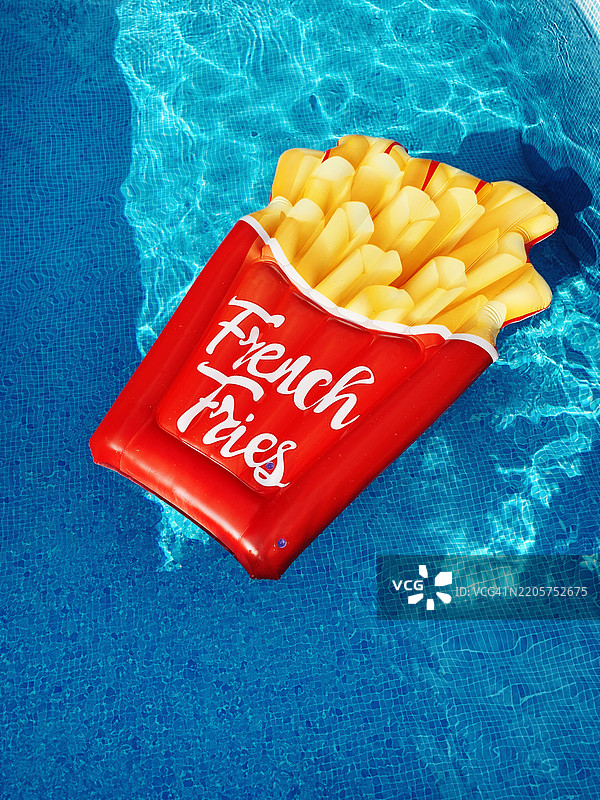 阳光明媚的夏日，游泳池中的薯条充气泳筏图片素材