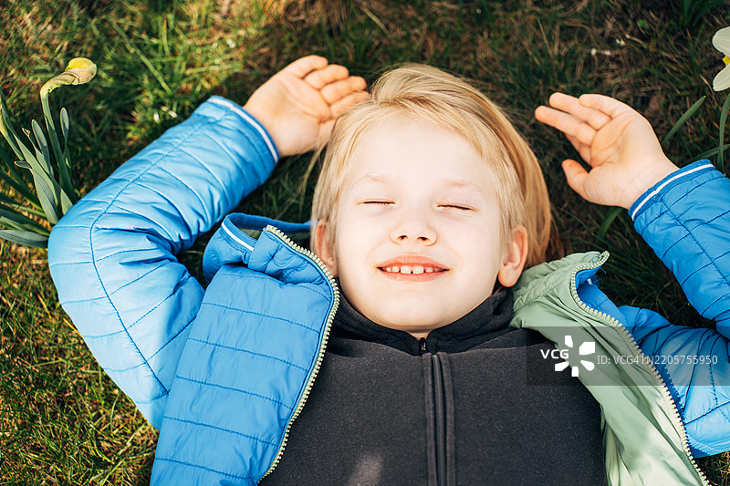 金发男孩躺在水仙花田里，面带梦幻的表情，享受春天的天气。图片素材