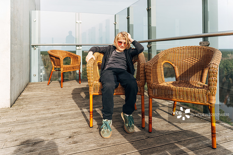 年轻男孩坐在屋顶露台上，享受阳光和城市景观图片素材