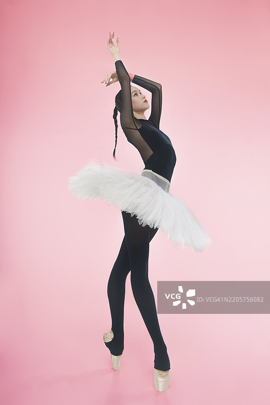 年轻的芭蕾舞者穿着黑色紧身衣和裙子，双臂在头顶上方展示外翻姿势。图片素材