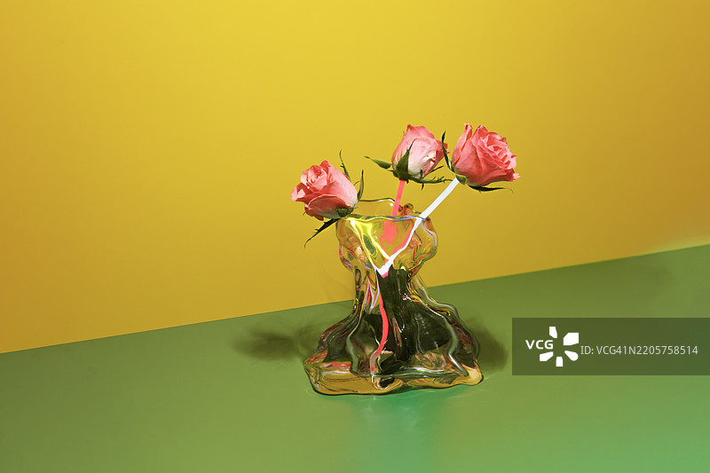 三朵粉色玫瑰在黄橄榄绿色背景上排成一行。玫瑰内部有可见的电线，将它们连接成一个人工系统。图片素材