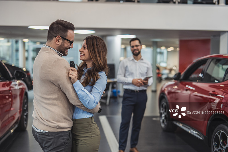幸福的情侣在汽车经销商处拥抱并握着新车钥匙图片素材