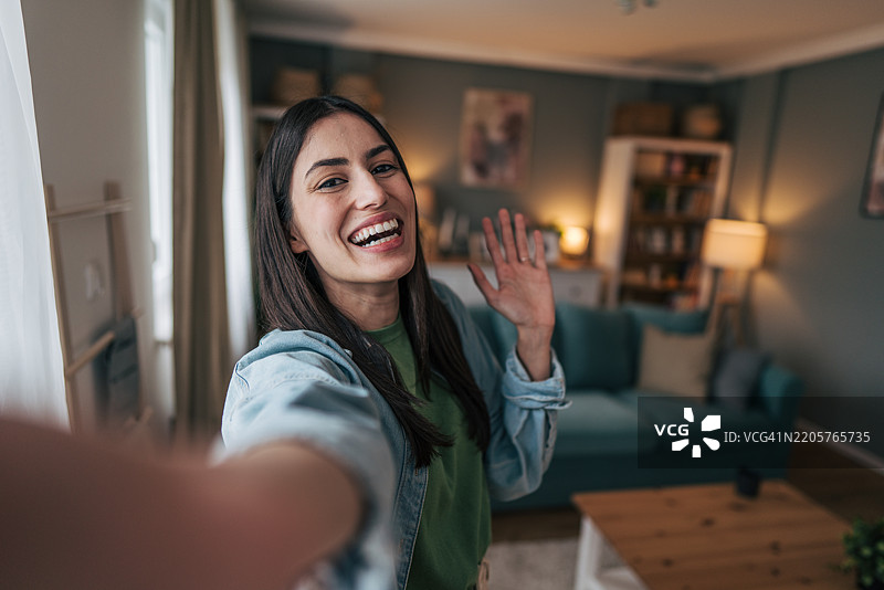 年轻女性在家中微笑着挥手自拍图片素材