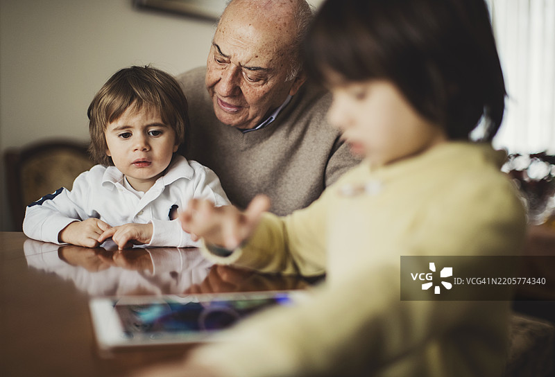 祖父与孙子们一起享受时光，他们正在使用平板电脑。图片素材