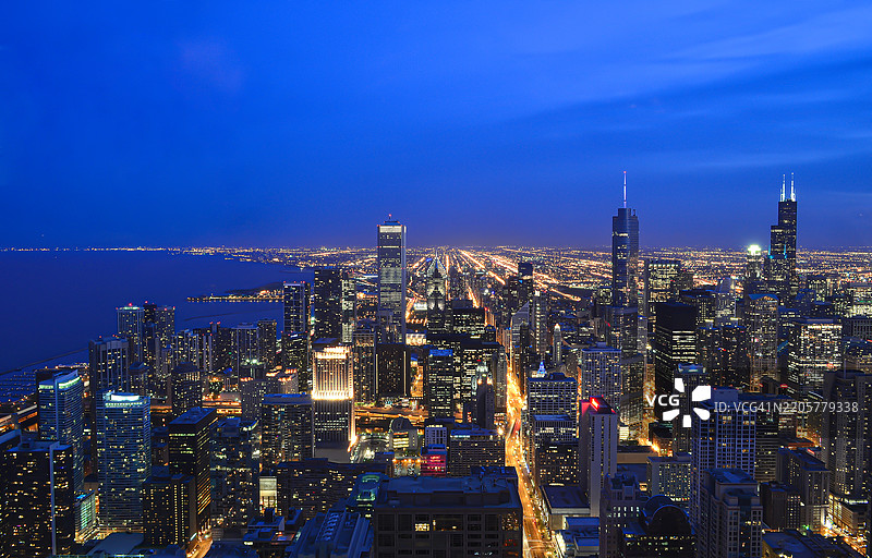 芝加哥天际线的航拍图，黄昏时分几乎入夜，标志性摩天大楼（威利斯大厦、安盛中心、特朗普大厦）在浪漫的天空下熠熠生辉，完美的蓝色密歇根湖水尽收眼底，位于美国伊利诺伊州芝加哥。图片素材