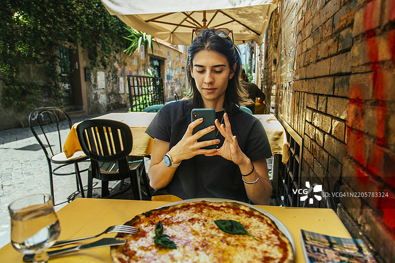 年轻女性在罗马特拉斯提弗列的户外餐厅桌子上拍摄披萨图片素材