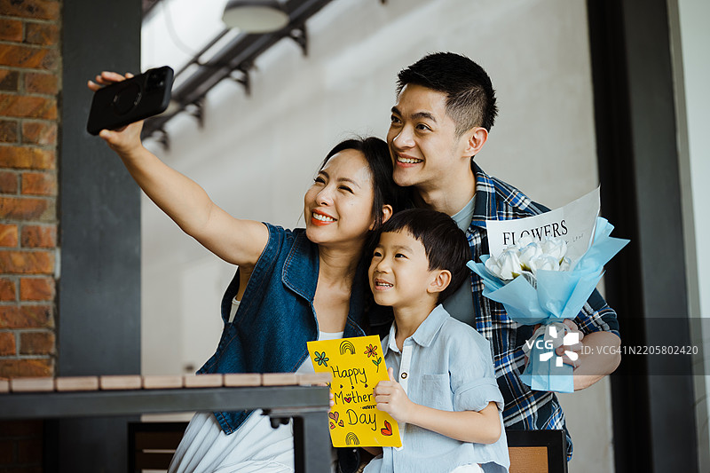 快乐的亚洲女性与家人一起自拍，手中拿着母亲节贺卡和鲜花图片素材