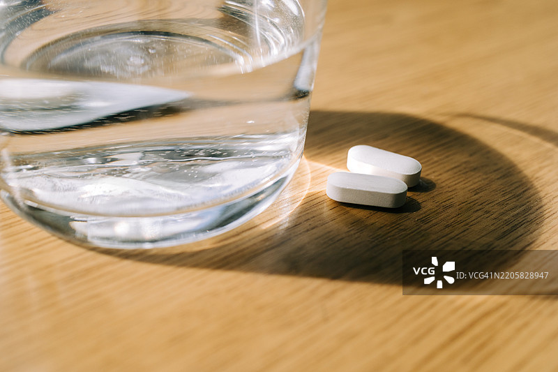 木桌上，水杯旁边放着药丸的特写镜头图片素材