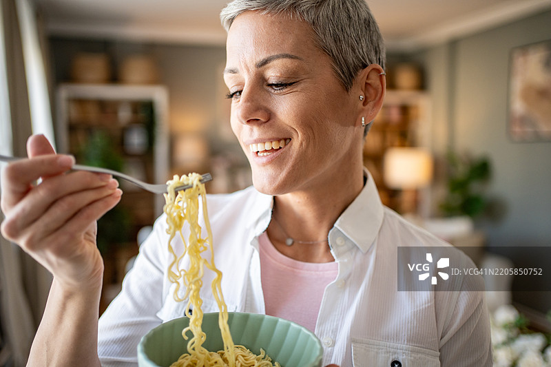 快乐的女人在家用叉子吃面条并微笑图片素材