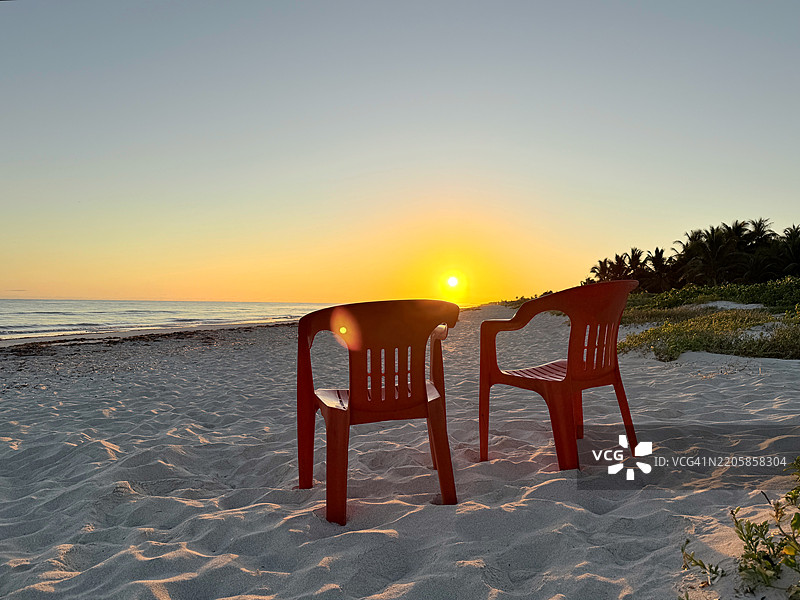 在墨西哥尤卡坦州的埃尔库约，日出时分的沙滩上，两把空塑料椅子。图片素材