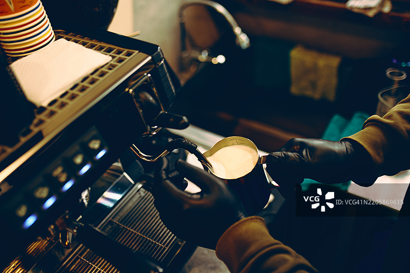 咖啡师在舒适的咖啡馆中使用意式咖啡机为咖啡准备牛奶图片素材