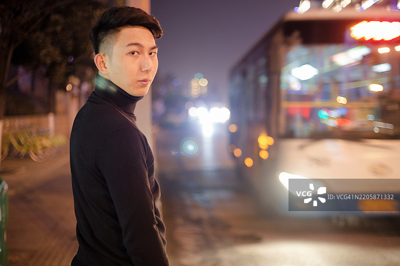 夜晚，一位亚洲男子站在街上等公交车。图片素材