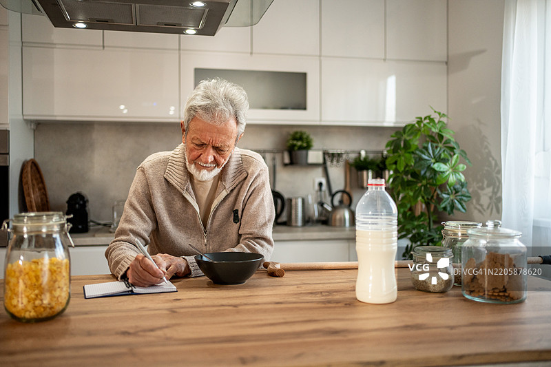 老年男子在厨房吃早餐时做笔记图片素材