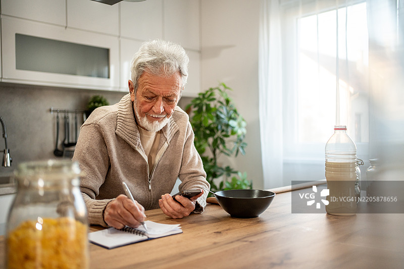 老年人在厨房用智能手机记笔记图片素材