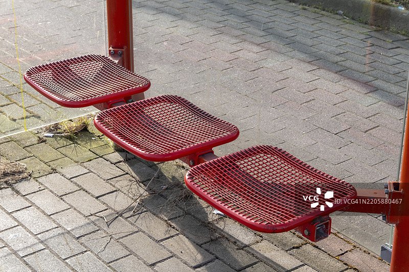 空荡荡的红色金属座椅在公交车站等待乘客休息，地点：德国北莱茵-威斯特法伦州博特罗普，欧洲图片素材