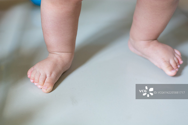 亚洲小女孩在妈妈的帮助下学习走路，第一次迈出步伐，家中卧室里可爱的摇摇欲坠的幼儿。快乐家庭的第一次步伐，亲子关系的概念。图片素材