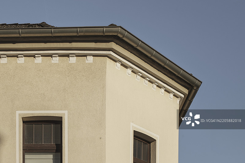 阳光照耀着一栋建筑的角落，雨水槽和装饰元素在晴朗的蓝天下，德国北莱茵-威斯特法伦州博特罗普。图片素材