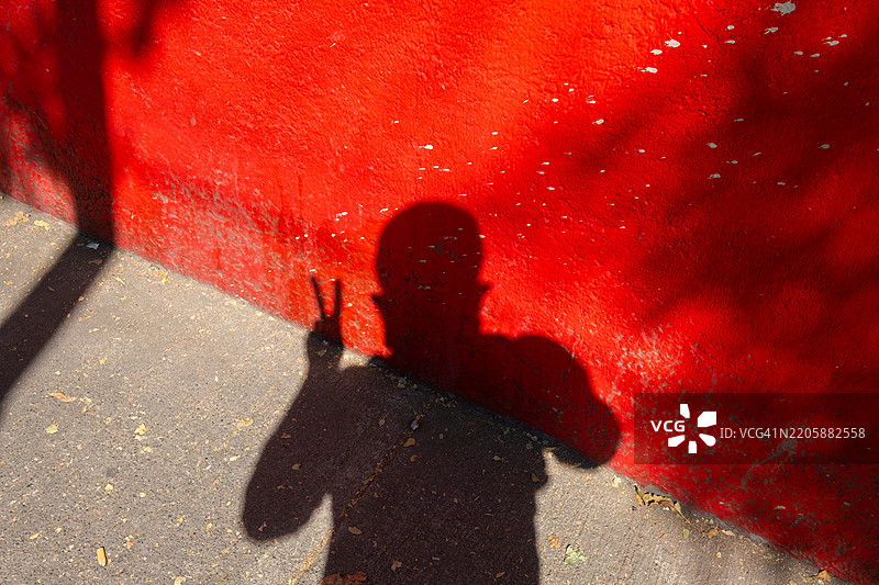 一个男人在墨西哥城的红色墙壁和人行道上低头做出和平手势的影子自画像图片素材