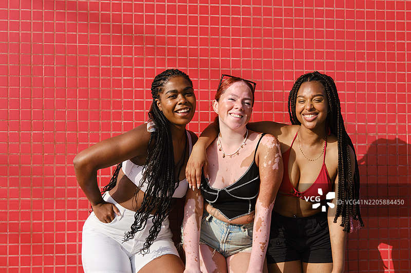 三位年轻女性在海滩上微笑着看向镜头，享受着快乐时光。图片素材