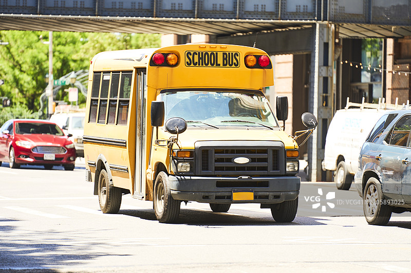 阳光明媚的城市里，一辆黄色校车正在行驶。图片素材