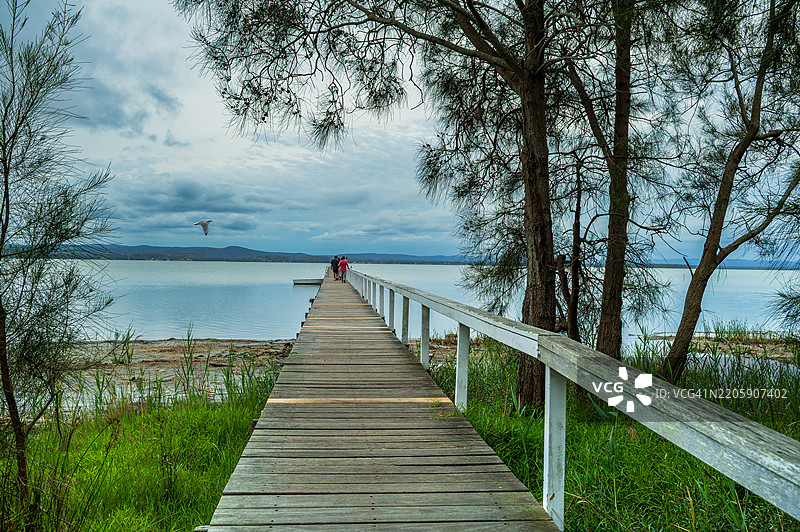 女人站在湖边的长码头上，背对着天空图片素材