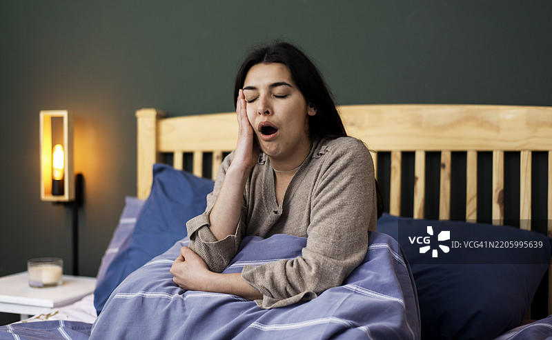 年轻女性在现代装饰的舒适卧室中迷迷糊糊地醒来图片素材