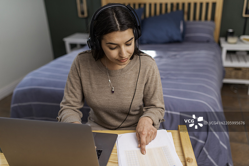 专注的女性在舒适的家庭工作空间中使用笔记本电脑，佩戴耳机图片素材