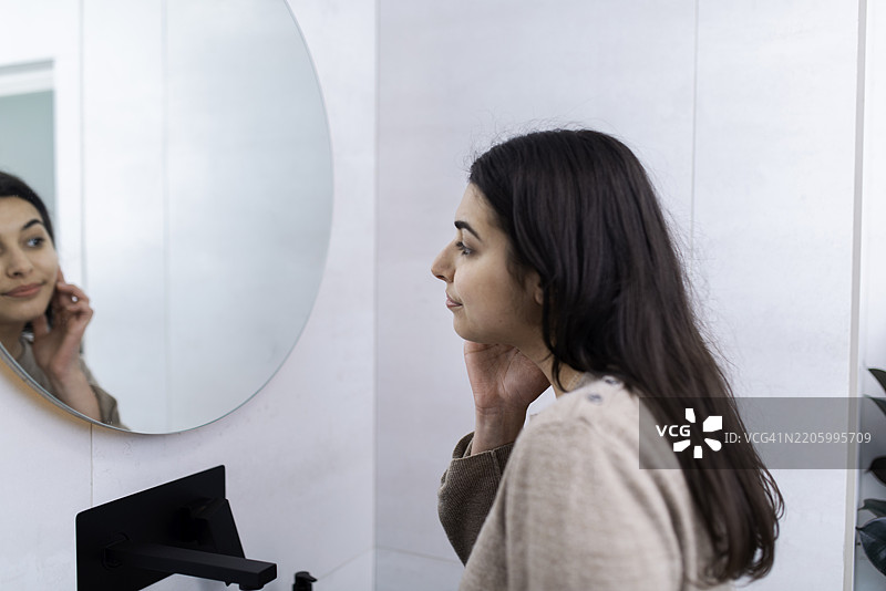 女人在现代浴室里站着，照镜子看自己图片素材