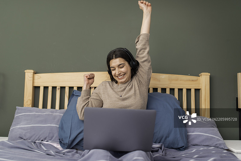 兴奋的女性在床上舒适地工作，享受在线成功图片素材