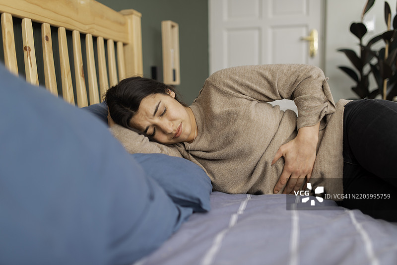 女性在放松的家居环境中躺在床上感受腹痛图片素材