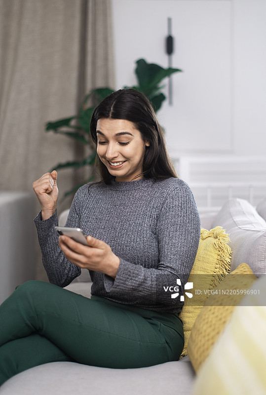 兴奋的女性在时尚的客厅环境中查看手机以获取好消息图片素材