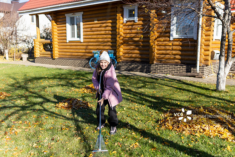 女孩在木屋前的院子里耙树叶图片素材