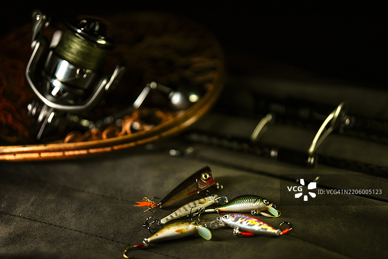 钓鱼卷线器、渔具和诱饵特写，静静地放在木制鱼网上，突显休闲钓鱼所用的工具。图片素材
