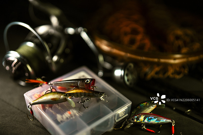钓鱼卷线器、齿轮和诱饵特写，静静地放在木制鱼网上，突显休闲钓鱼所用的工具。图片素材