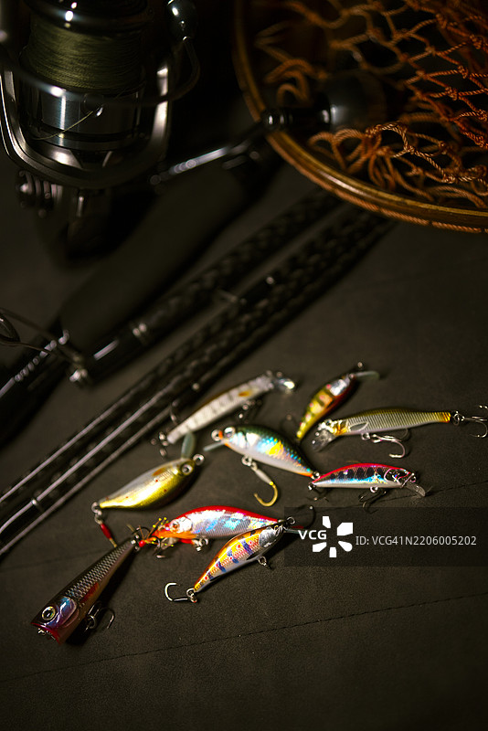 钓鱼卷线器、齿轮和诱饵特写，静静地放在木制鱼网上，突显休闲钓鱼所用的工具。图片素材