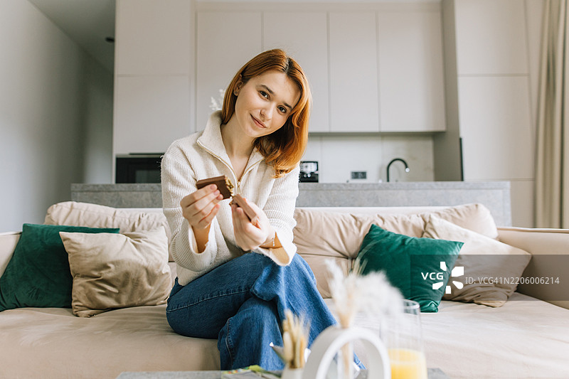 一位女士在沙发上坐着，撕下一块巧克力享用。图片素材