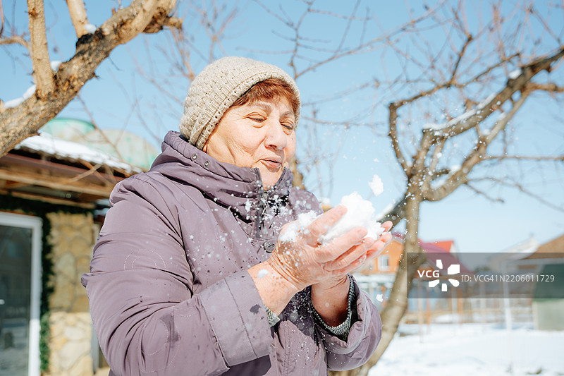 奶奶对雪感到高兴。对着他吹气。图片素材