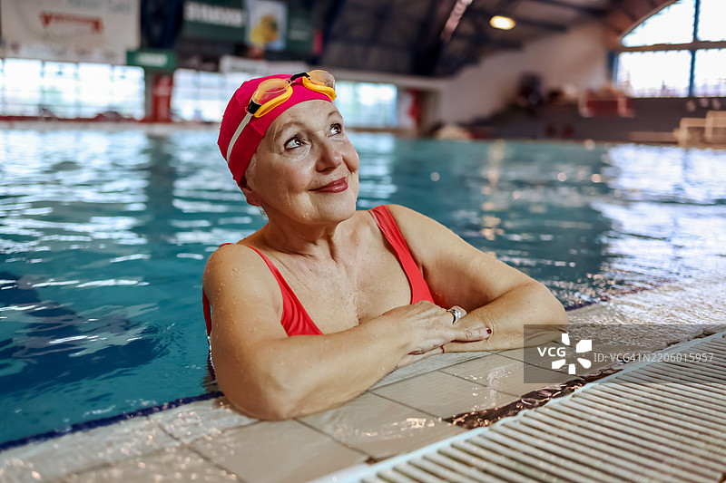 快乐的老年女性穿着运动风格的红色泳衣在游泳池中放松图片素材