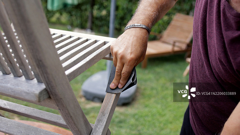 成熟男子在后院打磨一把旧木椅，成熟男子在给花园家具打磨前准备砂纸，修理工用砂纸去除木质表面的旧漆。图片素材