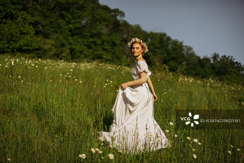 美丽的女孩在田野中手捧花束，头戴花环图片素材