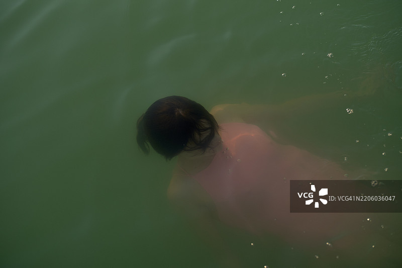 年轻女性在绿色浑浊的水中游泳，柔和的光线反射。德国勃兰登堡。图片素材