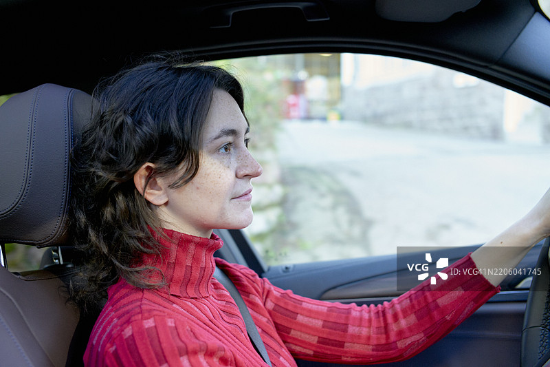 一位穿着红色毛衣的女性在城市中专注地驾驶着汽车图片素材