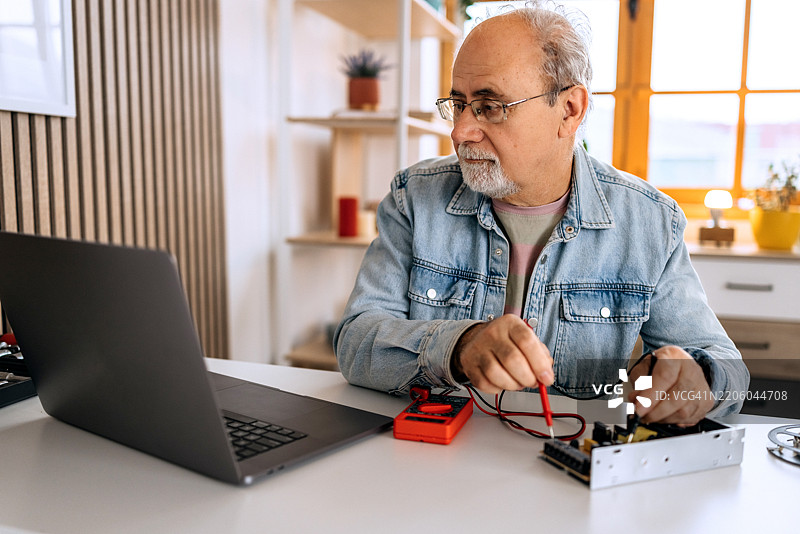 穿着休闲的老年男子在家中使用笔记本电脑按照说明书进行电子产品操作图片素材