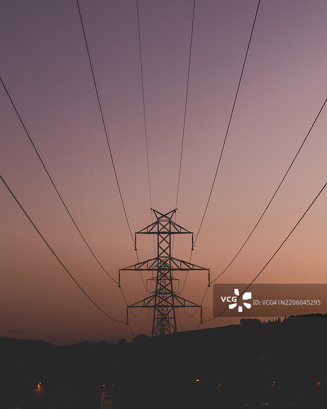 黄昏时分电力塔和电线的对称剪影。图片素材