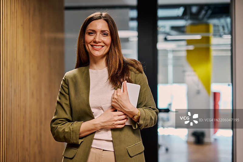 微笑的女商人在现代办公室走廊中手持平板电脑图片素材