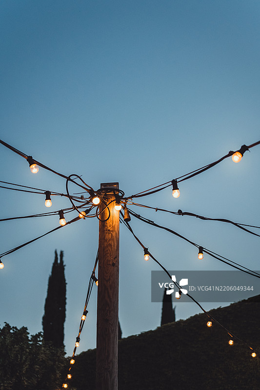 户外串灯照亮木柱，映衬黄昏的天空。图片素材