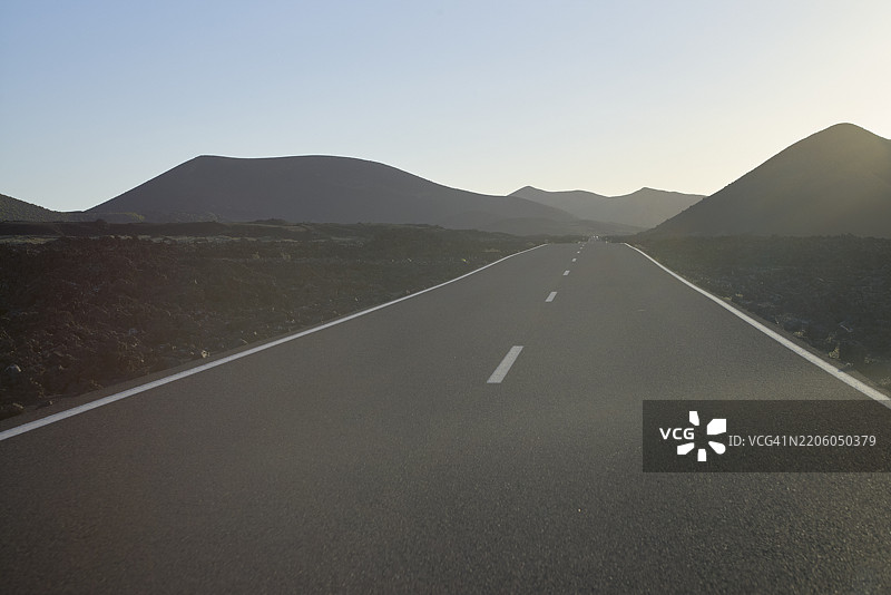 通往远处山丘的空旷道路，蓝天晴朗。西班牙兰萨罗特岛图片素材
